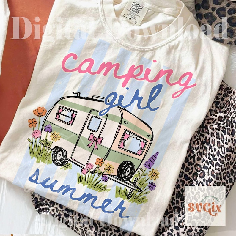 May include: Cream-coloured t-shirt with a camping theme. The design features a camper illustration with the words "Camping Girl Summer" in pink and blue. The camper is decorated with flowers and a pink bow.