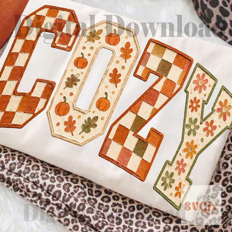 May include: A white fabric surface featuring the word COZY in large block letters. The C has an orange and white checkered pattern, the O features orange pumpkins and leaves, the Z has a checkered pattern, and the Y displays orange and green flowers.