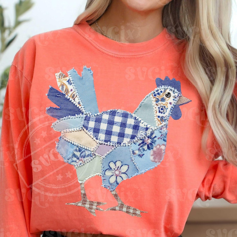 May include: Coral-colored sweatshirt featuring a patchwork chicken design. The chicken is composed of various blue and white patterned fabrics, including gingham and floral prints. The design is centered on the front of the long-sleeved shirt.