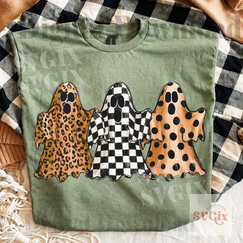 May include: An olive green short-sleeved t-shirt featuring a graphic print of three ghosts. The left ghost has a brown leopard print, the center ghost has a black and white checkerboard pattern, and the right ghost has a brown polka dot pattern.