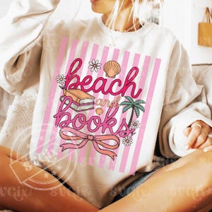 Puede incluir: Sudadera color crema con un dise&ntilde;o de rayas rosas y blancas. El gr&aacute;fico dice "beach and books" en escritura rosa, con ilustraciones de un libro, una concha, una palmera y flores.