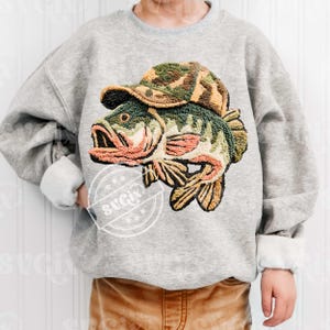 May include: A grey sweatshirt with an embroidered design of a largemouth bass wearing a camouflage hat. The fish has green, brown, and orange details. The sweatshirt has a crew neck and long sleeves with white cuffs.