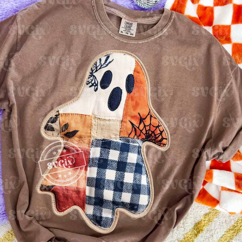 May include: Brown Comfort Colors XL t-shirt with a patchwork ghost design. The ghost features a white face with three dark blue eyes, orange and red accents, and a blue and white checkered bottom.