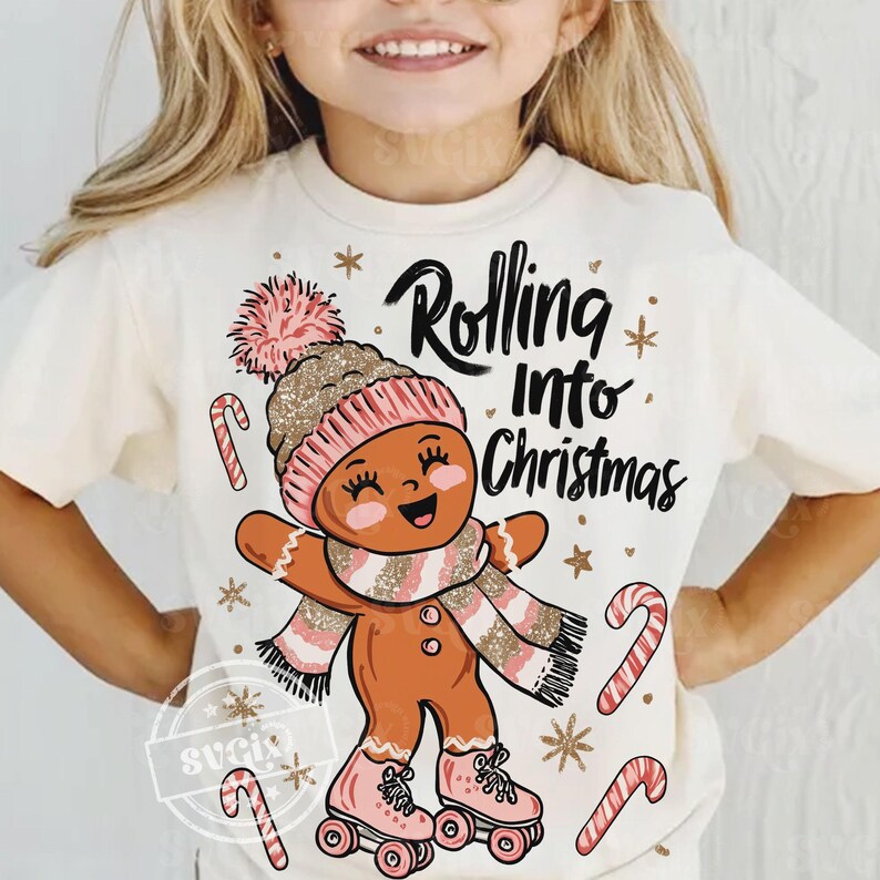 May include: Cream t-shirt with a gingerbread man design. The gingerbread man wears a pink and gold hat, scarf, and roller skates. The text "Rolling Into Christmas" is above the gingerbread man. Candy canes and snowflakes complete the festive design.