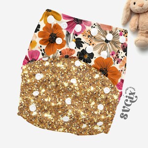 May include: Two cloth diapers. The top diaper has a floral pattern with orange, pink, and black flowers on a cream background. The bottom diaper is gold with glitter and white snaps. A stuffed bunny is in the background.