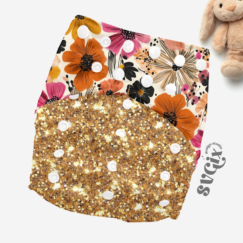 May include: Two cloth diapers. The top diaper has a floral pattern with orange, pink, and black flowers on a cream background. The bottom diaper is gold with glitter and white snaps. A stuffed bunny is in the background.
