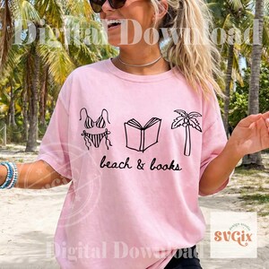 K&ouml;nnte beinhalten: Hellrosa T-Shirt mit schwarzer Grafik eines Bikinis, eines offenen Buches und einer Palme. Der Text "beach & books" steht darunter. Das T-Shirt hat einen l&auml;ssigen Stil.