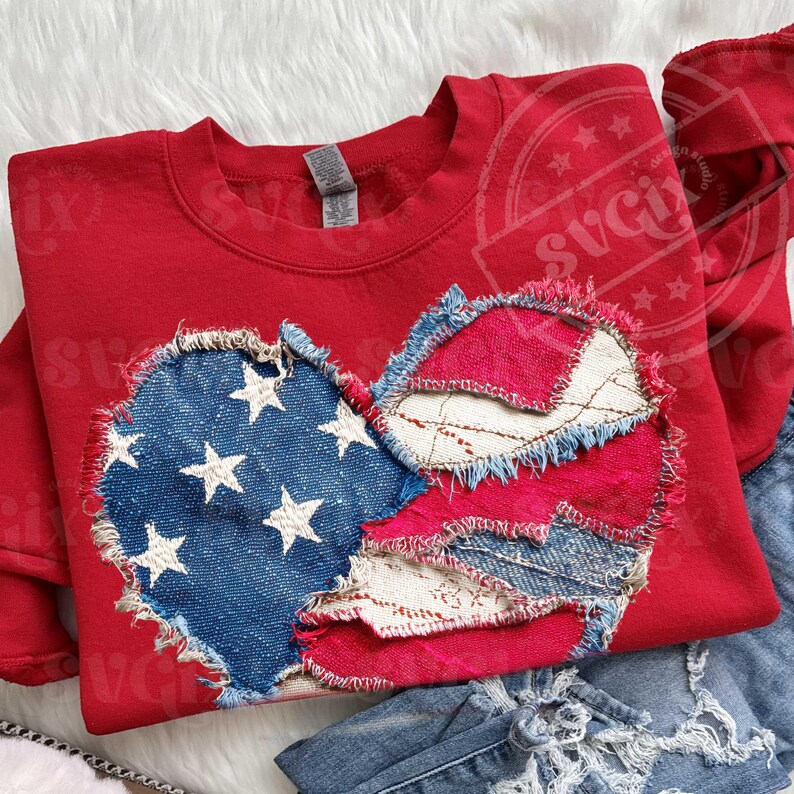 May include: A red sweatshirt featuring a distressed heart design. The heart is made of patches of blue denim with white stars, red fabric, and white lace-like fabric. The sweatshirt is paired with blue denim jeans.