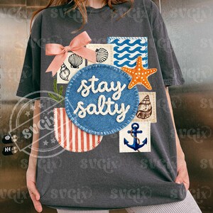 Peut inclure: T-shirt gris fonc&eacute; &agrave; th&egrave;me nautique. Il pr&eacute;sente un n&oelig;ud rose, des graphiques de coquillages et de vagues, et l'expression "stay salty" en &eacute;criture blanche. Comprend une &eacute;toile de mer orange et une ancre bleue.