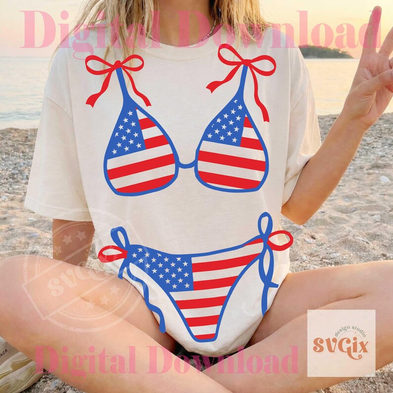 May include: A cream-colored t-shirt featuring a red, white, and blue bikini design. The bikini top and bottom are decorated with the American flag. The top has red bows on the straps, and the bottom has blue ties.