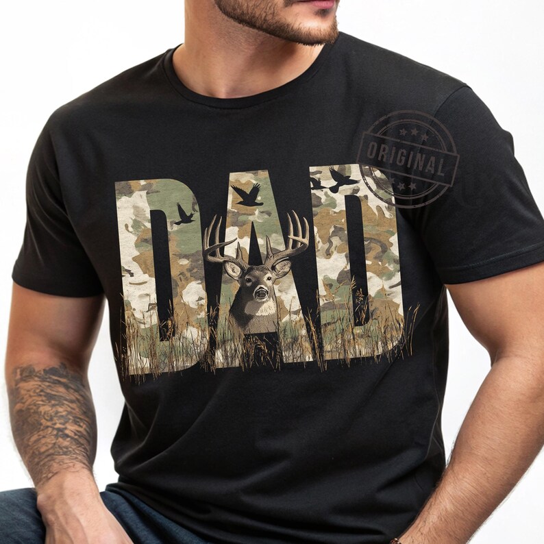 May include: A black t-shirt with a camouflage pattern and the word "DAD" in large letters. A deer with antlers is in the center of the word "DAD".