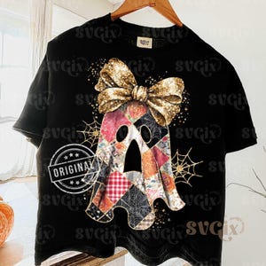 Op de afbeelding: Zwart T-shirt met een patchwork spookontwerp en een gouden paillettenstrik. De geest heeft bloemen- en ruitpatronen. Op het shirt staat het woord "ORIGINAL".