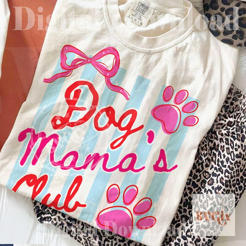 May include: Cream-colored t-shirt with the text "Dog Mama's Club" in red and pink script, accented with a pink bow and paw prints. Light blue vertical stripes add a playful touch to the design. The shirt is paired with leopard print pants.