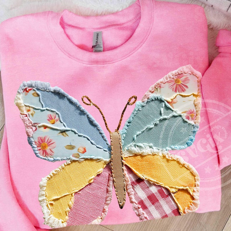 May include: A pink sweatshirt featuring a large, colorful butterfly applique. The butterfly wings are made of patchwork fabric in shades of blue, yellow, pink, and white, with floral and gingham patterns. The butterfly's body is a tan color.
