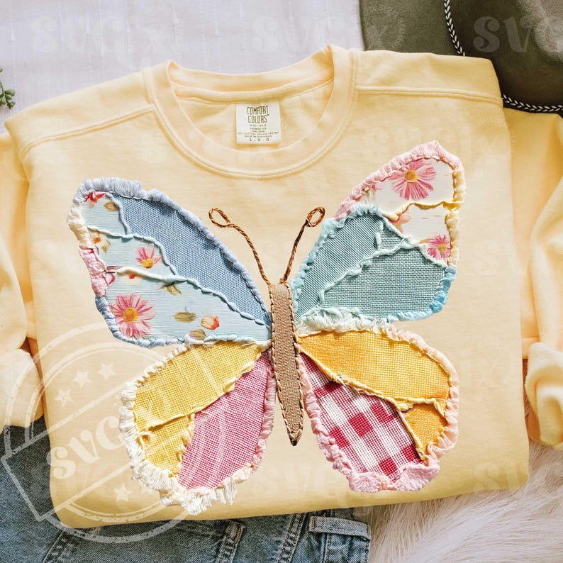 May include: A light yellow sweatshirt with a large, colorful butterfly applique. The butterfly wings are made of patchwork fabric in shades of blue, pink, yellow, and green, with floral and gingham patterns. The sweatshirt has a crew neck and long sleeves.
