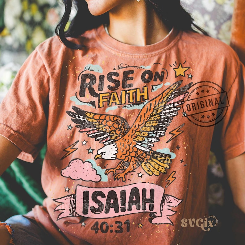Puede incluir: Camiseta de color coral con un dise&ntilde;o de un &aacute;guila volando. El dise&ntilde;o incluye las palabras "RISE ON FAITH" sobre el &aacute;guila e "ISAIAH 40:31" debajo. La palabra "ORIGINAL" est&aacute; estampada en el lado derecho.