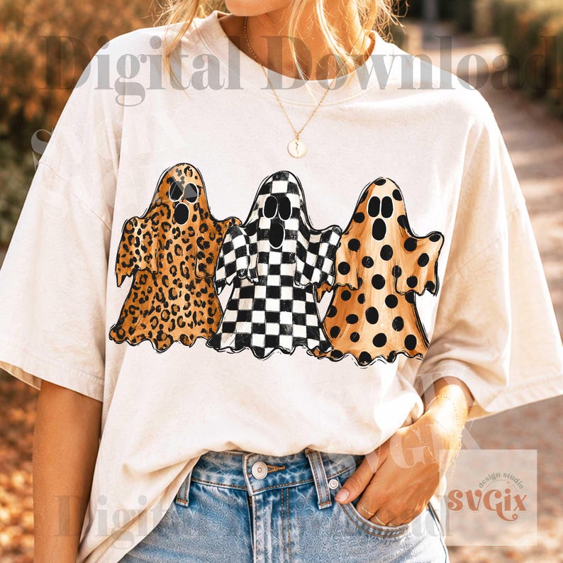 May include: A cream-colored short-sleeve t-shirt featuring a graphic of three ghosts. The left ghost has a brown leopard print, the middle ghost has a black and white checkerboard pattern, and the right ghost has a brown polka dot pattern.