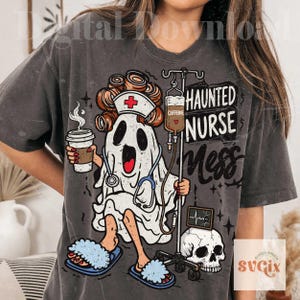 Puede incluir: Una camiseta gris carb&oacute;n con el gr&aacute;fico de un fantasma con rulos, una cofia de enfermer&iacute;a y un estetoscopio. El fantasma sostiene una taza de caf&eacute; y est&aacute; junto a un soporte de suero con la etiqueta CAFFEINE, una calavera y el texto HAUNTED NURSE MESS.