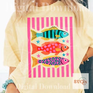 May include: A light yellow t-shirt featuring a graphic of three colorful fish within a pink striped frame. The fish are blue, red, and pink, each with unique patterns and star accents. The design is a digital download.