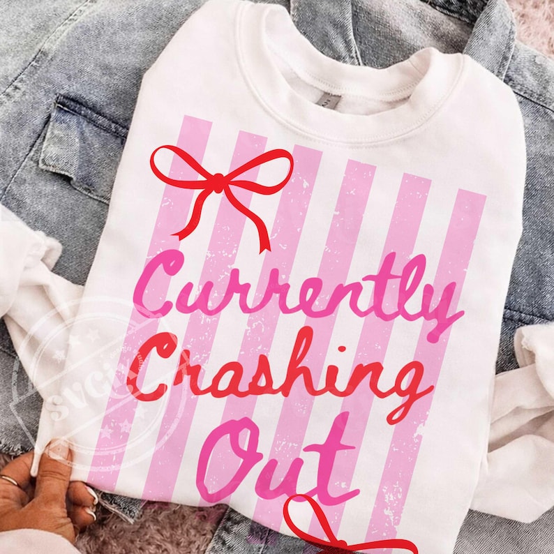 May include: White sweatshirt with pink vertical stripes and the text "Currently Crashing Out" in pink and red. A red bow is at the top. The sweatshirt is displayed on a denim jacket.