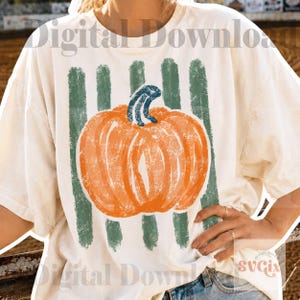 May include: An off-white short-sleeve t-shirt featuring a graphic of an orange pumpkin with a blue stem centered over vertical sage green brushstrokes. The text Digital Download is printed in a light gray font across the top of the shirt.