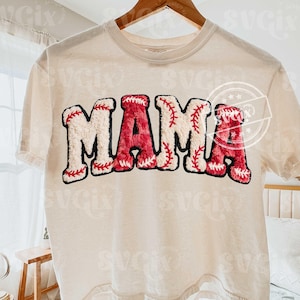 May include: Cream-colored t-shirt with the word "MAMA" in a baseball-themed design. The letters are white with red baseball stitching and a red baseball texture. The shirt is hanging on a wooden hanger.