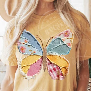 May include: Yellow t-shirt featuring a patchwork butterfly design. The butterfly has wings in various colors and patterns, including blue floral, yellow, pink gingham, and light blue. The butterfly's body is a tan color.