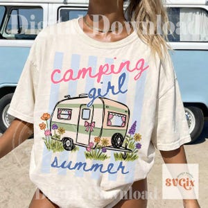 May include: Cream t-shirt featuring the words "camping girl summer" and a camper graphic with flowers. The text is pink and blue, set against a light blue striped backdrop.
