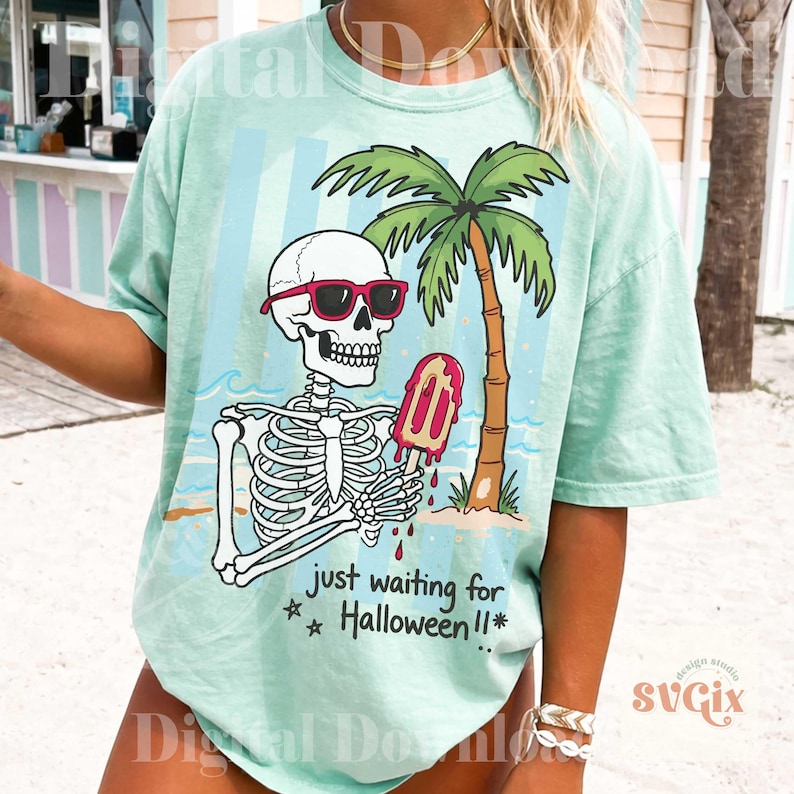 May include: Mint green t-shirt featuring a skeleton wearing sunglasses and holding a melting popsicle on a beach with a palm tree. The text "just waiting for Halloween!!" is printed below the skeleton. The shirt has a relaxed fit.
