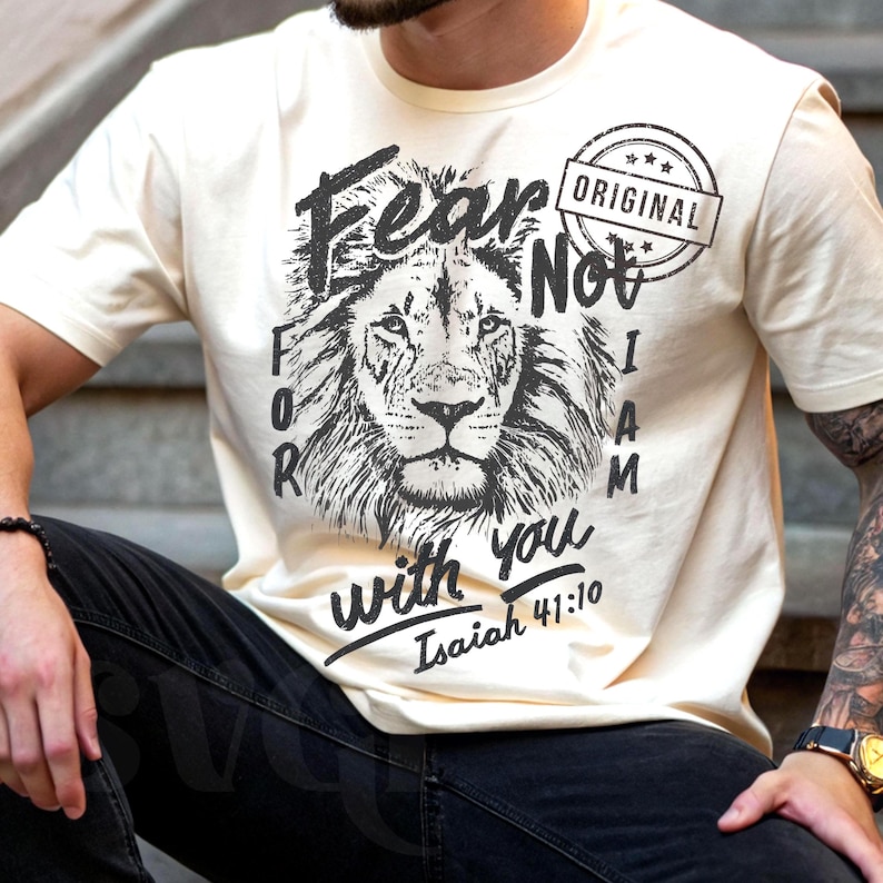 Puede incluir: Camiseta color crema con un gr&aacute;fico detallado en blanco y negro de una cabeza de le&oacute;n. La camiseta incluye el texto "Fear Not, I Am with you" y "Isa&iacute;as 41:10" en una fuente estilizada, con un sello "Original".