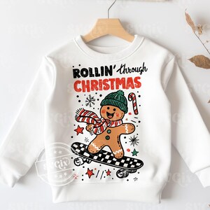 May include: White sweatshirt with a gingerbread man on a skateboard. The gingerbread man has a green hat and a red and white scarf. The text "ROLLIN' through CHRISTMAS" is above the gingerbread man.
