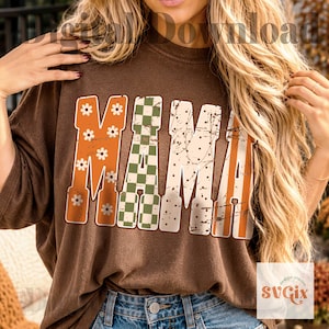 May include: A brown short-sleeve t-shirt featuring the word MAMA in large block letters. Each letter has a distinct pattern: the first M has white daisies on orange, the A has a green checkerboard, the second M has black dots, and the final A has orange stripes.
