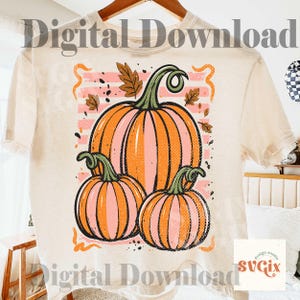 May include: Cream-colored t-shirt featuring a graphic of three pumpkins in shades of orange and pink. The pumpkins are set against a pink and white striped background with autumn leaves. The words "Digital Download" are printed on the top and bottom of the shirt.