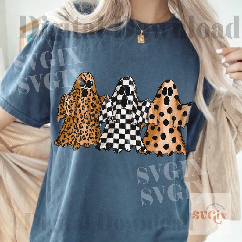 May include: A blue short-sleeve t-shirt featuring a graphic of three ghosts. The left ghost has a brown leopard print, the middle ghost has a black and white checkerboard pattern, and the right ghost has a brown polka dot pattern.