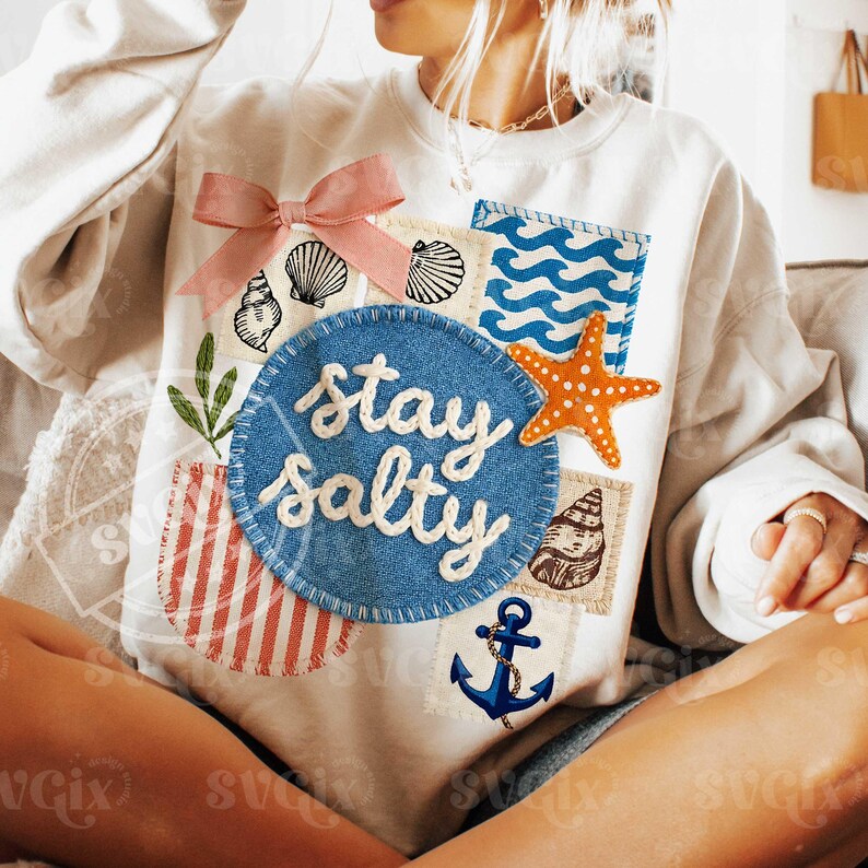 Peut inclure: Sweat-shirt cr&egrave;me avec un motif patchwork. Il pr&eacute;sente un n&oelig;ud rose, des coquillages, une &eacute;toile de mer et l'expression "stay salty" en &eacute;criture blanche sur un cercle bleu. D'autres patchs incluent une ancre et un motif de vagues.