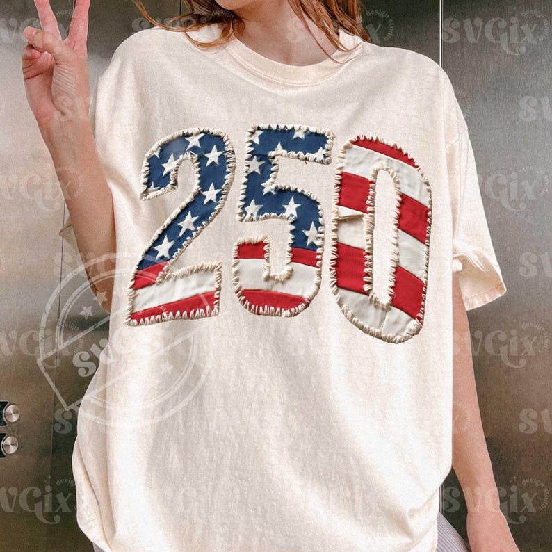 Może przedstawiać: Kremowa koszulka z numerem "250" w patriotycznym wzorze. Numery wykonane są w stylu patchwork, z wykorzystaniem kolor&oacute;w czerwonego, białego i niebieskiego z amerykańskiej flagi. Koszulka ma klasyczny okrągły dekolt i kr&oacute;tkie rękawy.