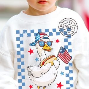 May include: White sweatshirt with a cartoon duck wearing sunglasses and a red, white, and blue baseball cap. The duck is holding a hot dog and a small American flag. The background is a blue and white checkered pattern with red stars.