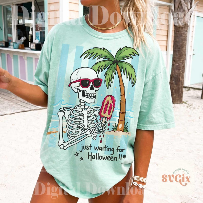 May include: A light green t-shirt featuring a skeleton wearing sunglasses and holding a melting popsicle. A palm tree and the text "just waiting for Halloween!!" are also on the shirt. The shirt has a relaxed fit.
