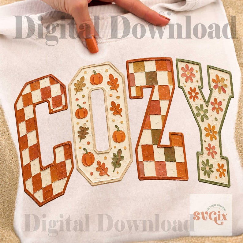 May include: A white sweatshirt featuring the word COZY in large block letters. The C is orange and white checkered, the O has orange pumpkins and leaves, the Z is orange and brown checkered, and the Y has orange and green flowers.