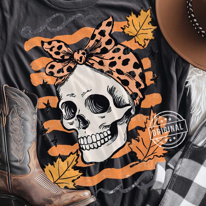 Puede incluir: Camiseta gris oscuro con una calavera que lleva un pa&ntilde;uelo con estampado de leopardo. El dise&ntilde;o incluye rayas naranjas, hojas de oto&ntilde;o y estrellas. Una bota de vaquero y un sombrero son visibles en el fondo. La camiseta tiene un sello "ORIGINAL".