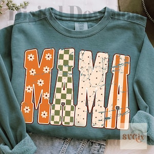 May include: A teal crewneck sweatshirt featuring the word MAMA in large block letters. Each letter has a distinct pattern: orange with white flowers, green and white checkerboard, cream with brown dots, and orange vertical stripes.
