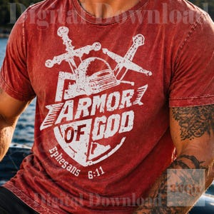K&ouml;nnte beinhalten: Rotes T-Shirt mit einem verblichenen wei&szlig;en Aufdruck. Der Aufdruck zeigt einen Helm, gekreuzte Schwerter und den Text "ARMOR OF GOD" mit "Ephesians 6:11" darunter. Das T-Shirt hat einen Vintage-Look.