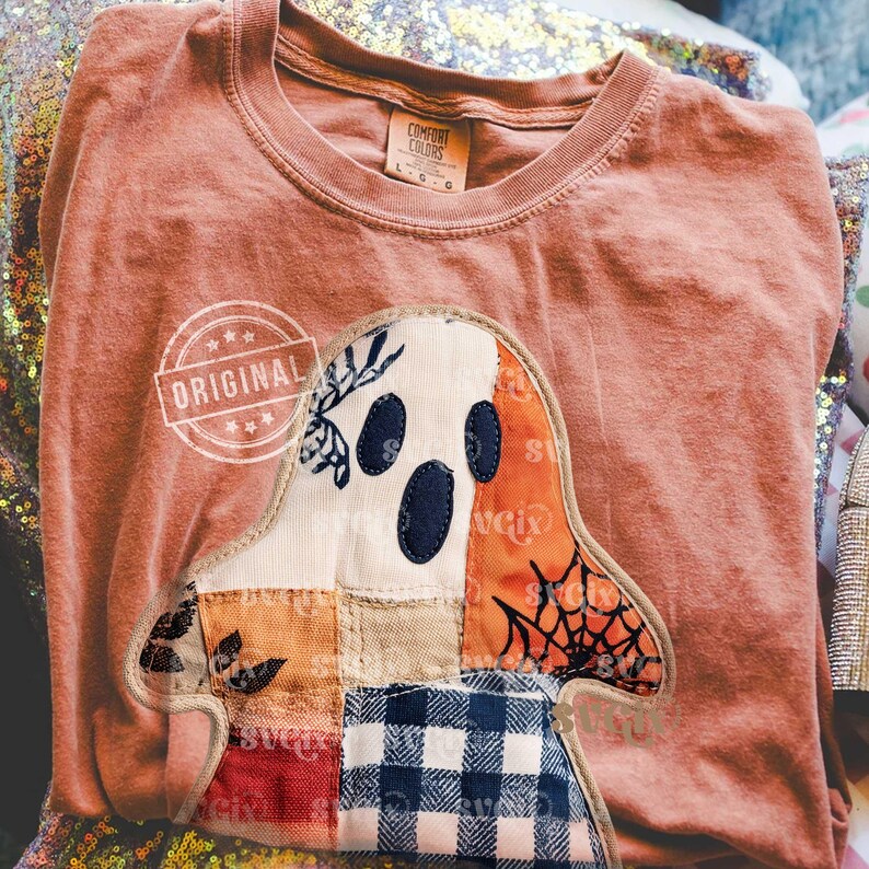 May include: A coral-colored Comfort Colors t-shirt featuring a patchwork ghost design. The ghost has a white face with navy blue eyes and mouth, and is decorated with orange, blue, and red fabric. The word "ORIGINAL" is stamped on the shirt.