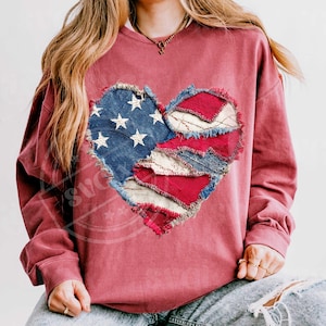 May include: A maroon sweatshirt with a heart-shaped design made from patches of denim and red and white fabric. The denim patch features white stars, reminiscent of the American flag. The heart's edges are frayed, giving it a rustic appearance.