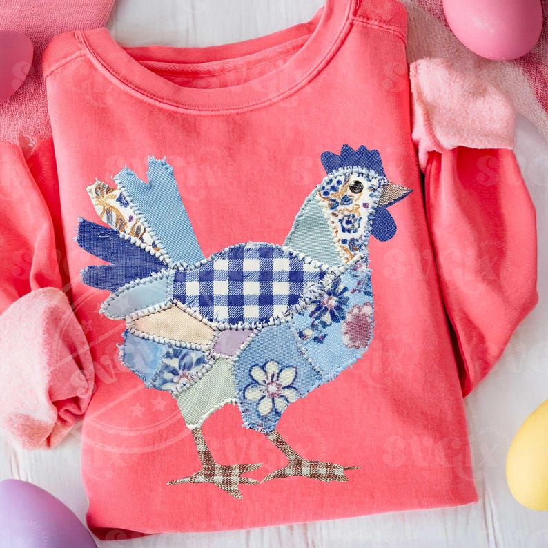 May include: A coral-colored long-sleeved shirt featuring a patchwork chicken design. The chicken is composed of various blue patterned fabrics, including floral and gingham patterns. The shirt has a crew neck and long sleeves, perfect for casual wear.