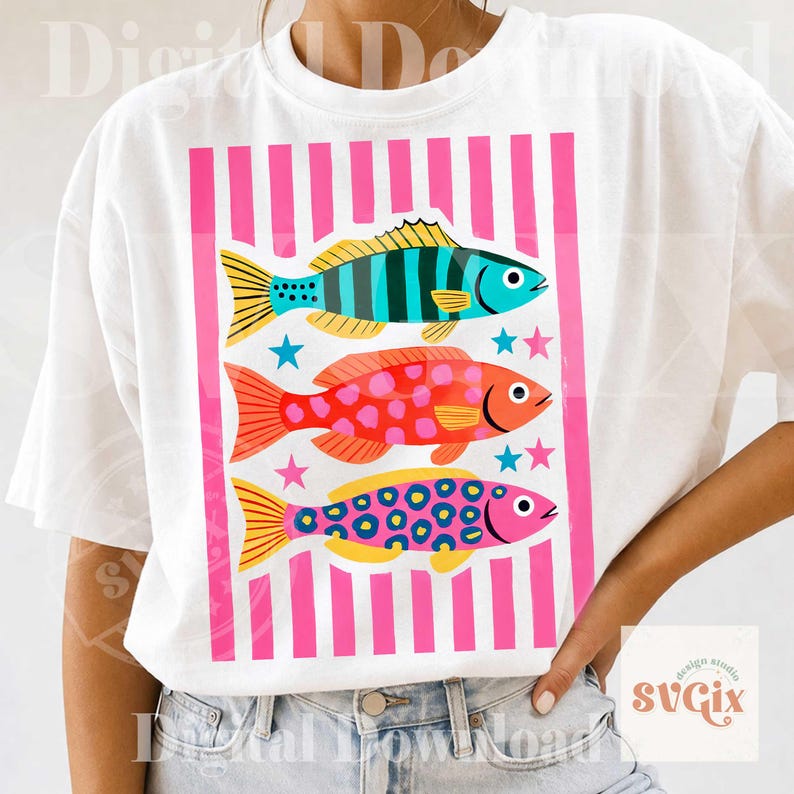 May include: White t-shirt featuring a colorful graphic of three stylized fish. The fish are in shades of blue, red, and pink, with yellow accents and star details. The design is set against a pink striped background.
