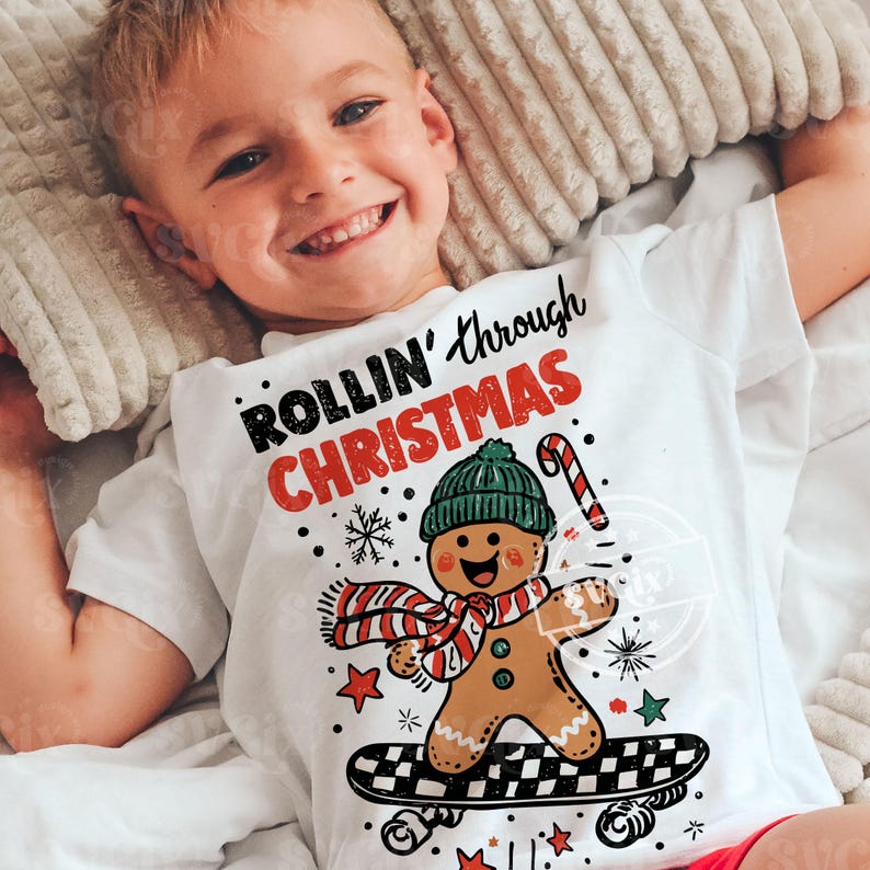 May include: A white t-shirt with the text "ROLLIN' through CHRISTMAS" in black and red. The shirt features a gingerbread man wearing a green hat and a red and white scarf, skateboarding. Includes snowflakes, stars, and a candy cane graphic.