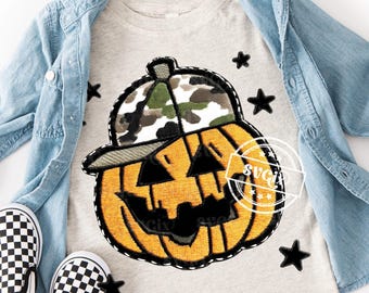 Op de afbeelding: Lichtgrijs t-shirt met een lachende pompoen met een camouflage baseballpet. De pompoen is oranje met zwarte accenten en is omgeven door zwarte sterpatches. Een lichtblauwe spijkerjas en schoenen met schaakbordpatroon maken de look compleet.