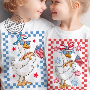 May include: Two children wearing white t-shirts with a red, white, and blue checkered pattern. The shirts feature a cartoon goose wearing sunglasses, a red, white, and blue bandana, and holding a hot dog. The goose is also holding a small American flag. The shirts are a fun and festive way to celebrate the 4th of July.