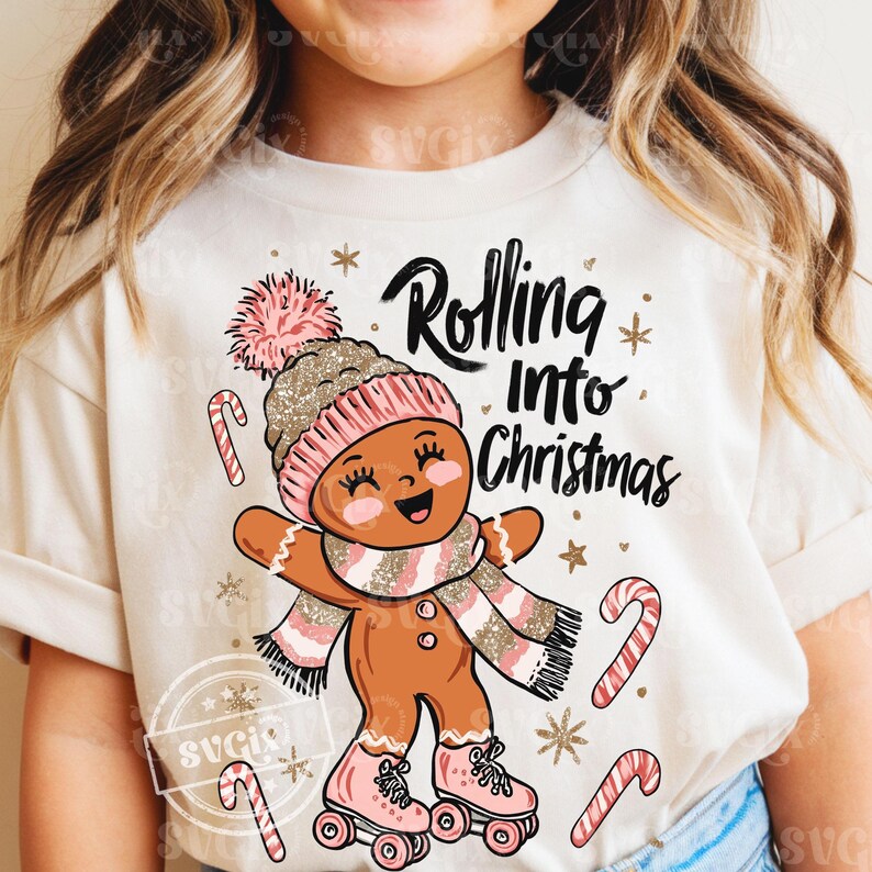 May include: A cream t-shirt with a gingerbread person wearing a pink and gold hat, scarf, and roller skates. The text "Rolling Into Christmas" is above the gingerbread person, with candy canes and stars scattered around.